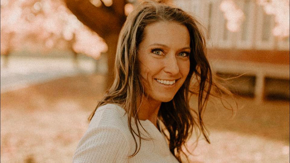 Rebecca Bliefnick smiles in sepia tone photo in front of large tree