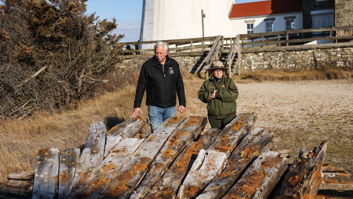 Tony Femminella, executive director of the Fire Island Lighthouse Preservation Society, and Betsy DeMaria, museum technician with Fire Island National Seashore, stand next to a section of the hull of a ship believed to be the SS Savannah which wrecked in 1821 off Fire Island on Jan. 27, 2023. The section now rests alongside the Fire Island lighthouse. 