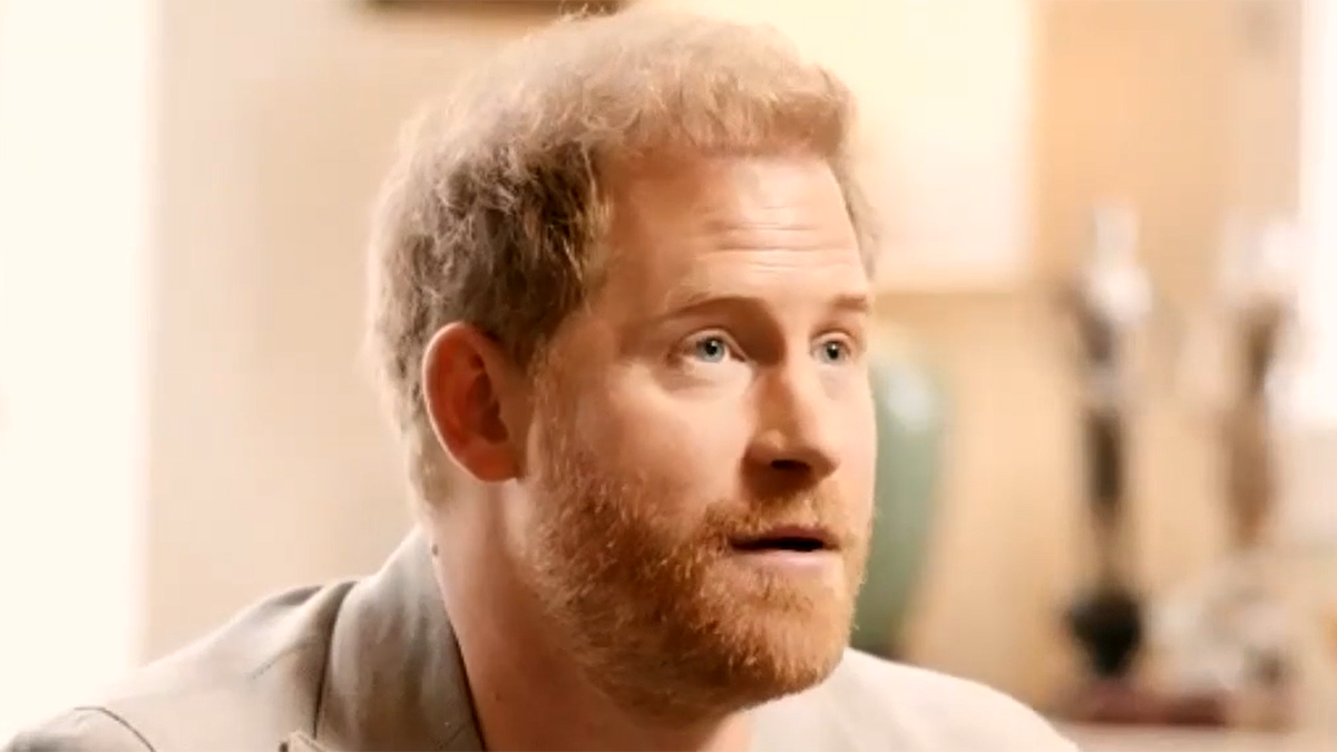 Prince Harry in a grey shirt and light brown jacket speaks during a conversation with Dr. Gabor Maté