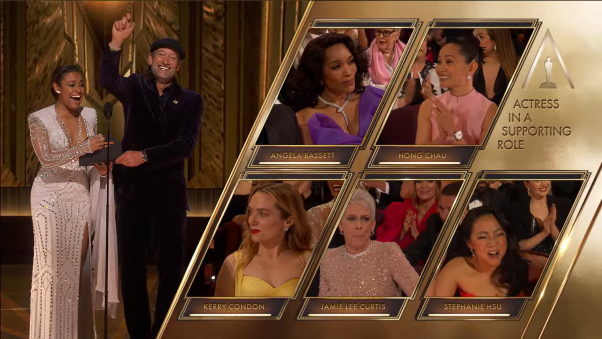 A wide screen shows presenters Ariana DeBose and Troy Kotsur announcing Jamie Lee Curtis as the winner of the Best Supporting Actress Award, to which she looks stunned in her chair, surrounded by heads of all the other nominees