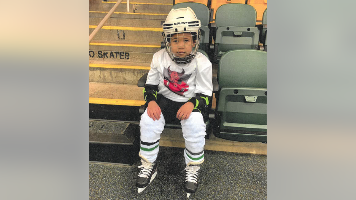 Zohar in a white hockey uniform and helmet sits in a chair