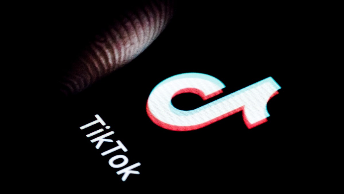 O logotipo do aplicativo TikTok em um telefone e um dedo