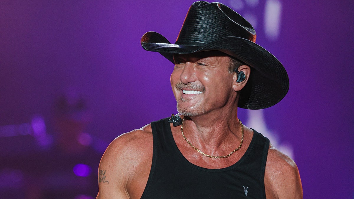 Tim McGraw performs live wearing a black tank top and matching cowboy hat