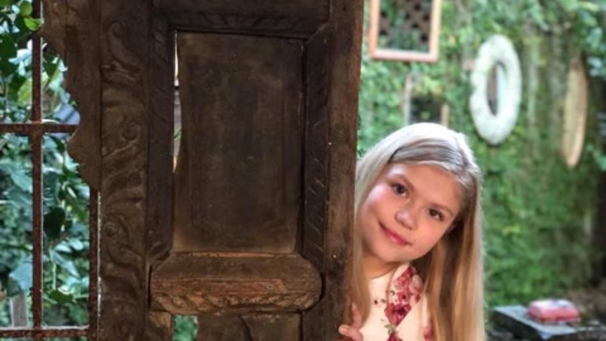 Tristyn Bailey as a little girl peers from behind a door.