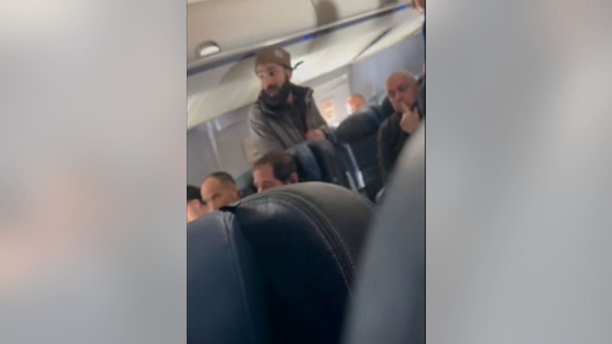Man standing up in an airplane yelling at staff.