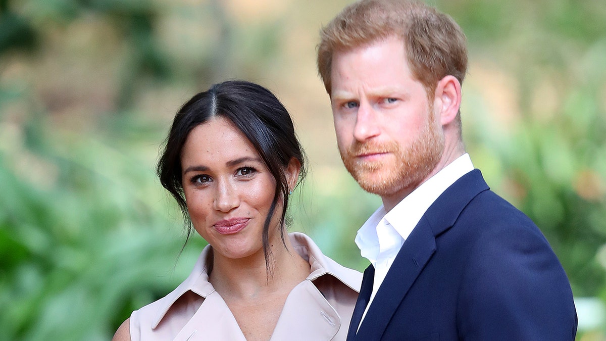Meghan Markle smiles while Prince Harry looks serious while they stare at the camera