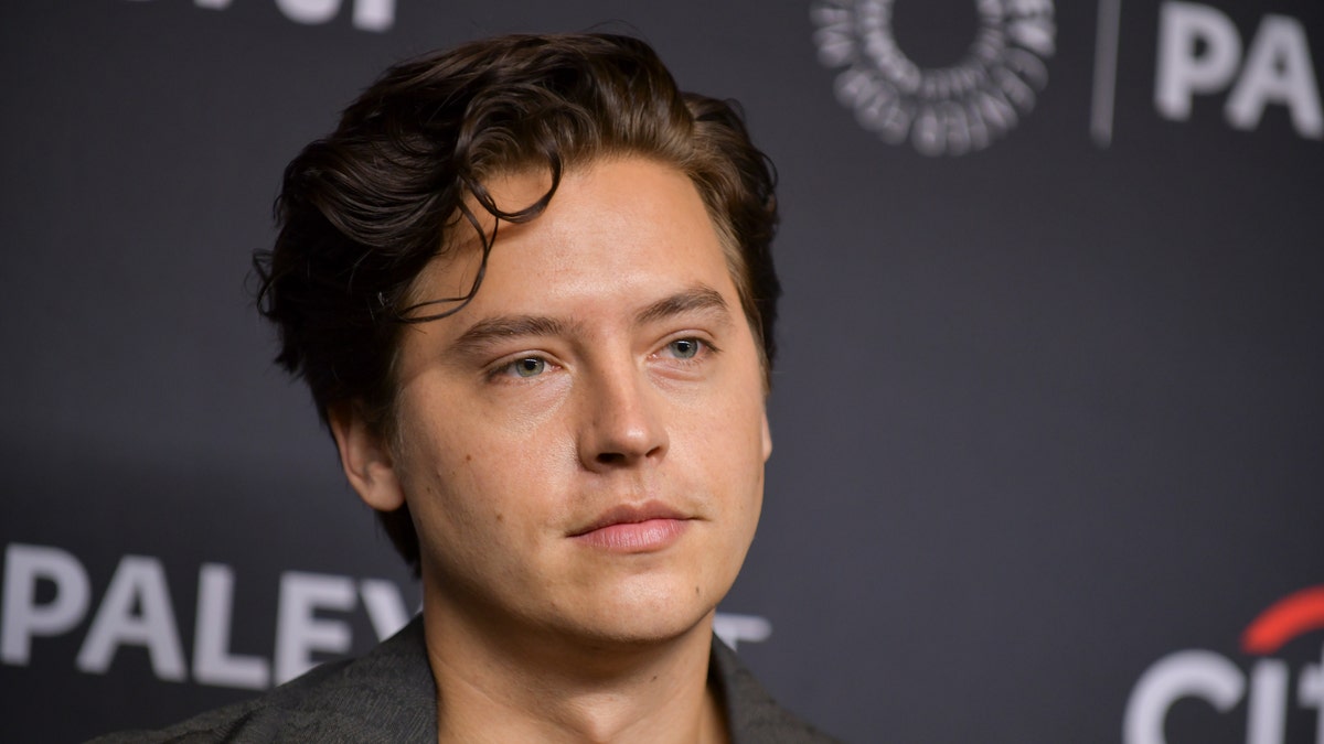 Cole Sprouse looks somewhat solemn as he poses for a photo at an event.