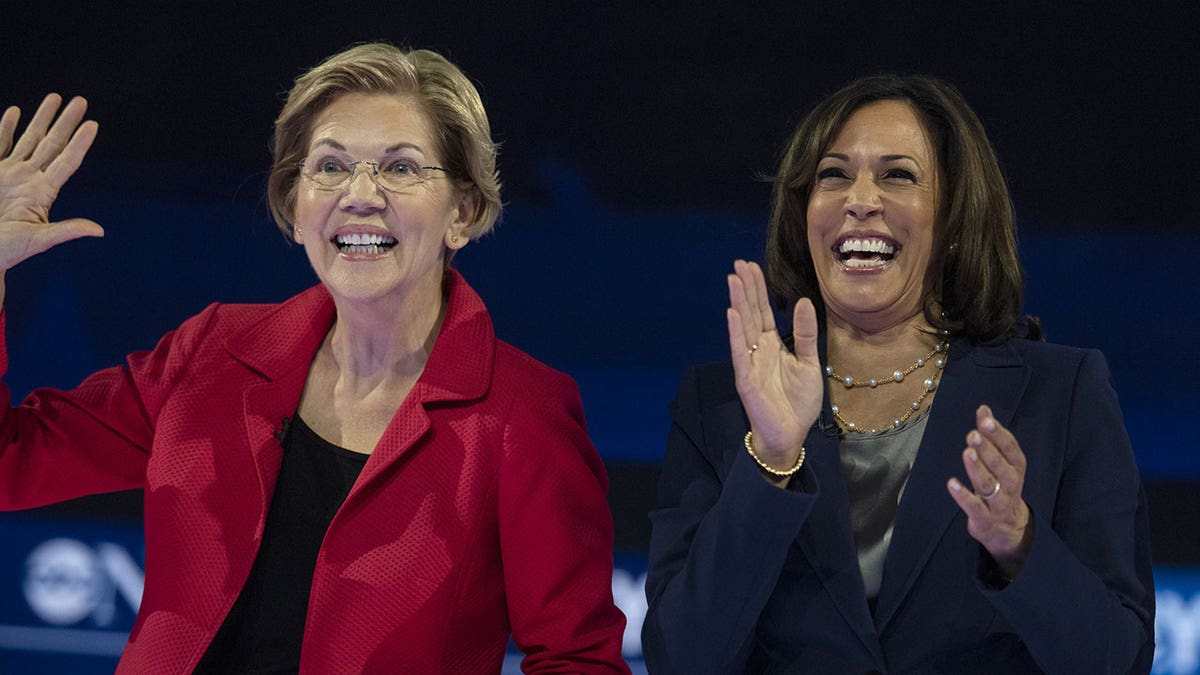 Sen Elizabeth Warren smiles alongside Kamala Harris who is clapping onstage