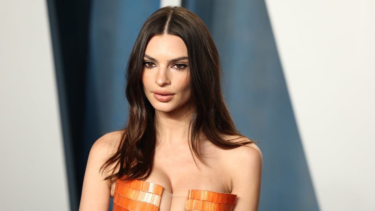 Emily Ratajkowski poses on red carpet in revealing orange dress.