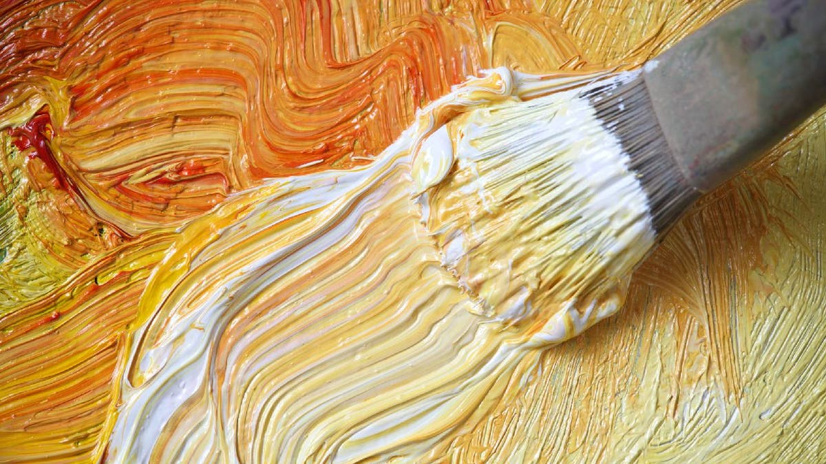 Paint brush spreads orange and white paint on surface