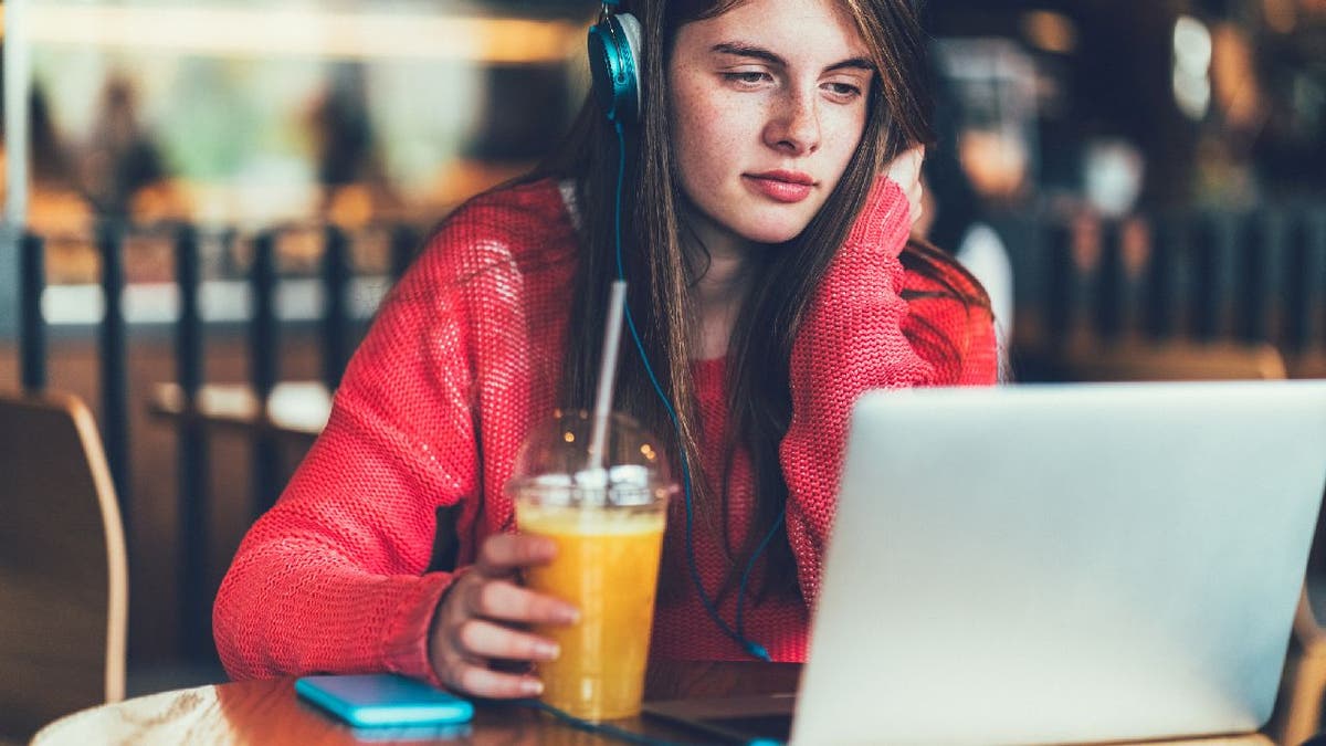 Teenage girl using laptop with drink in hand