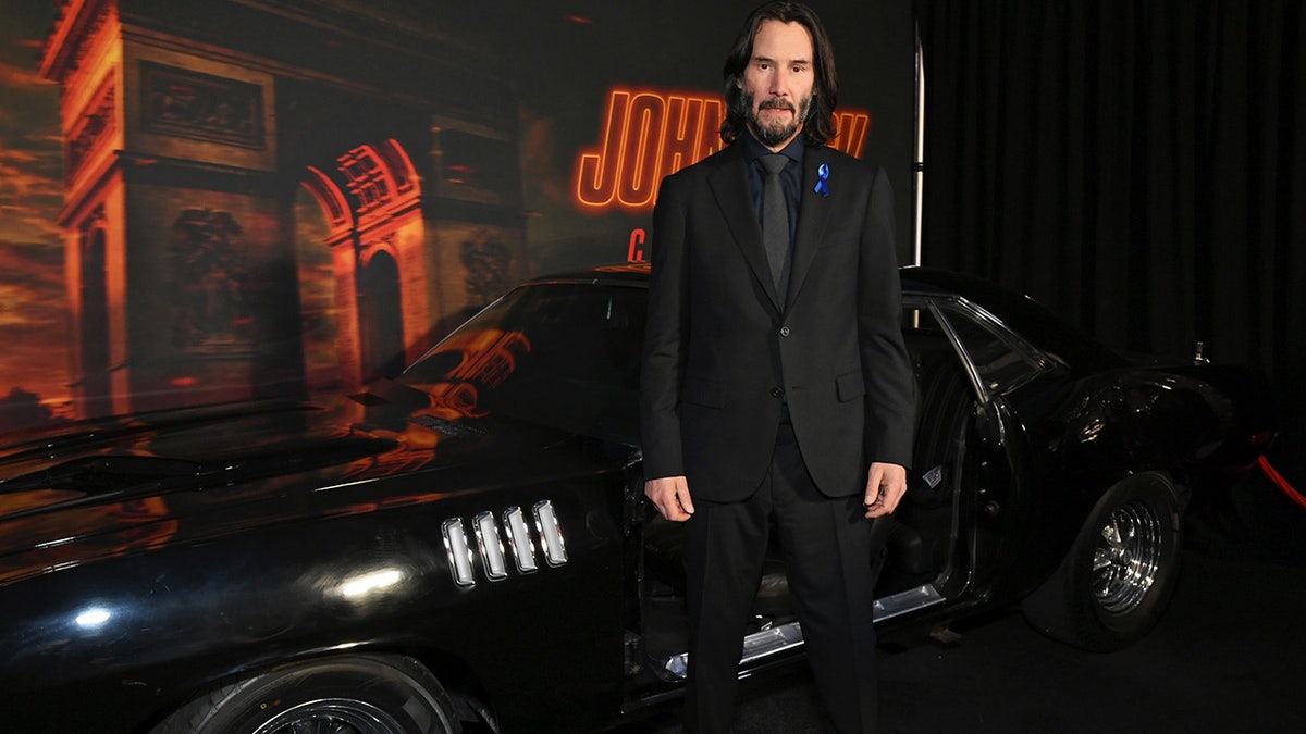 Keanu Reeves wears suit with blue ribbon in honor of late co-star Lance Reddick.