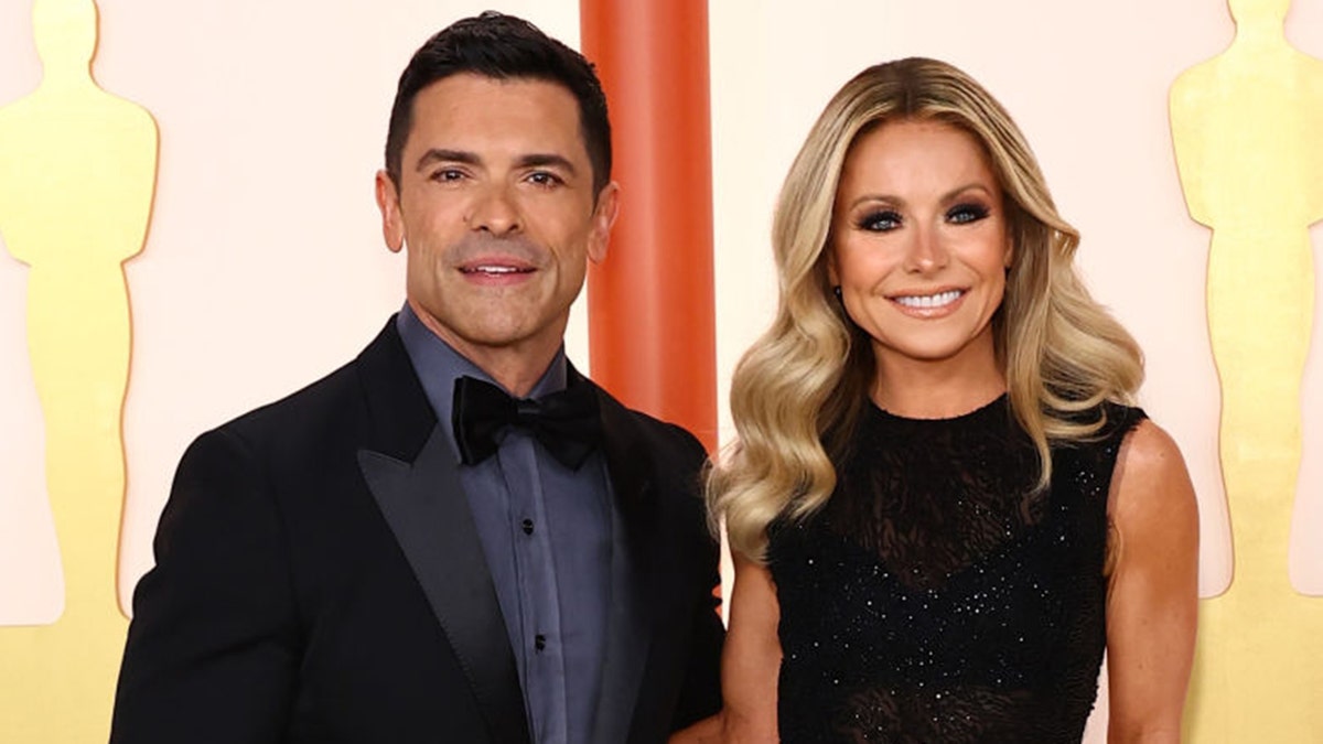 Mark Consuelos in a black velvet tuxedo jacket and blue shirt and black bow-tie stands next to Kelly Ripa in a black dress and dark eye-makeup at the Oscars