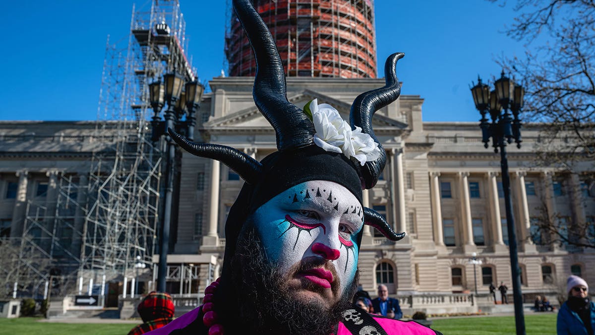 Protestor with face paint and head piece stands in front of Kentucky Capitol building