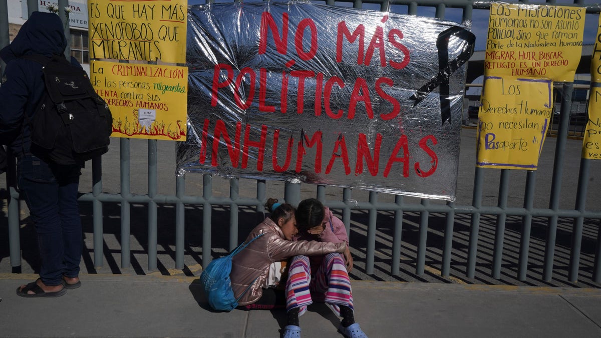 A pair of Venezuelan sisters comfort each other sitting on a sidewalk outside an immigration detention center where dozens of migrants fearing deportation set mattresses ablaze, starting a fire that killed dozens in Ciudad Juarez, Mexico, Tuesday, March 28, 2023. 