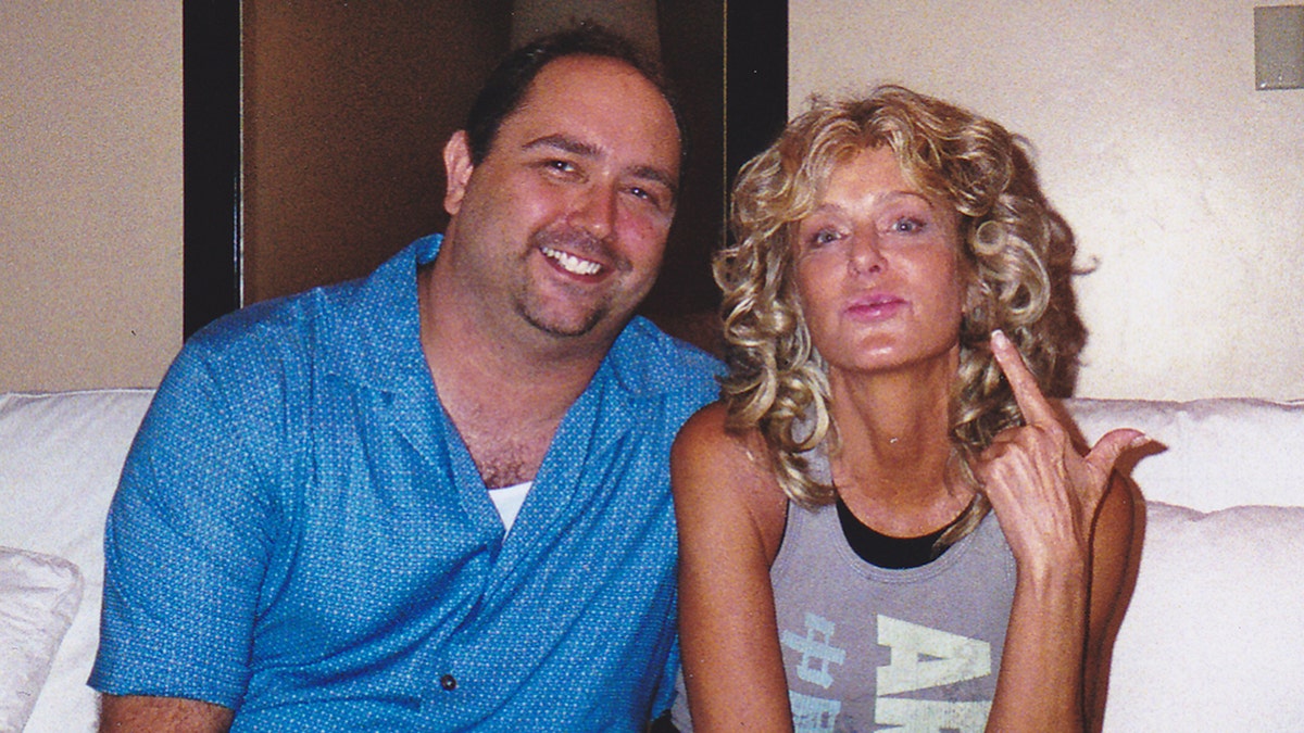 Mike Pingel wearing a blue blouse with a white shirt smiling next to Farrah Fawcett wearing a grey tank top