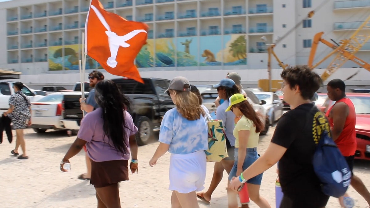 A group of college students holding a Texas longhorn flag walk to the beach. 