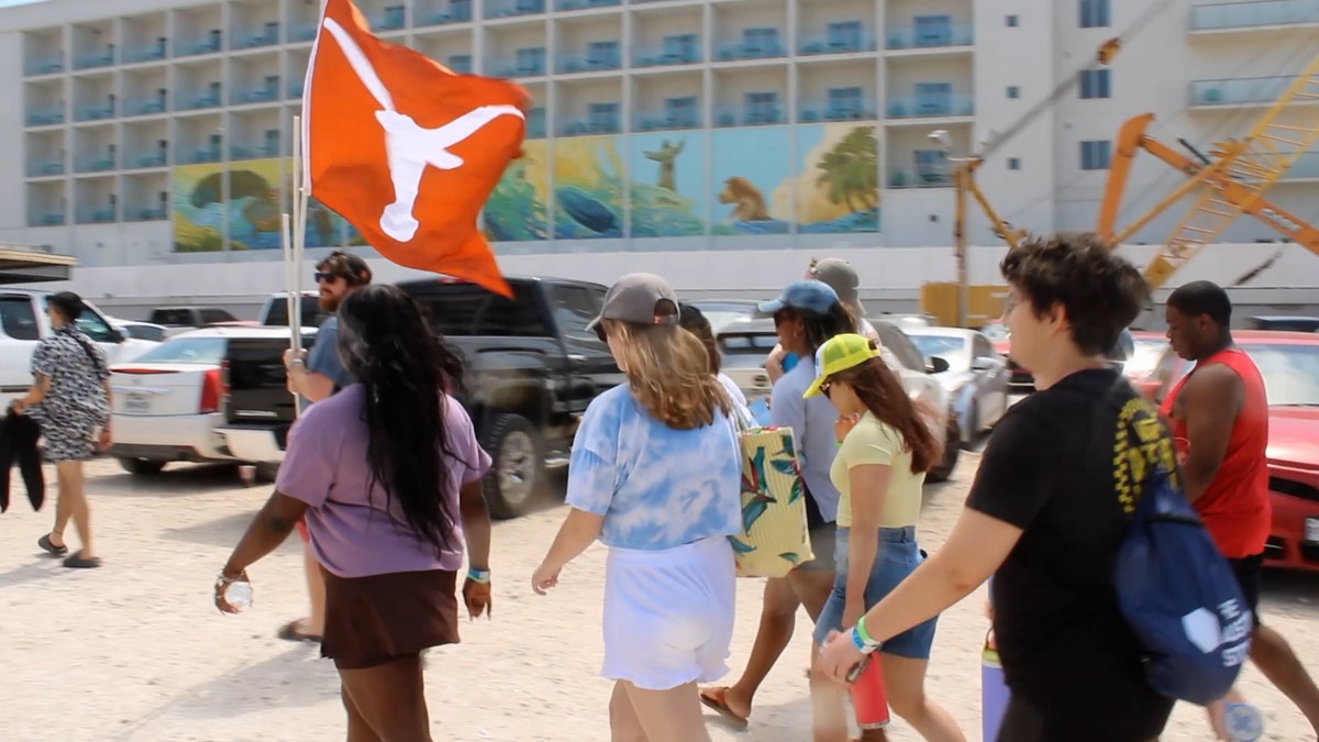 A group of college students holding a Texas longhorn flag walk to the beach.