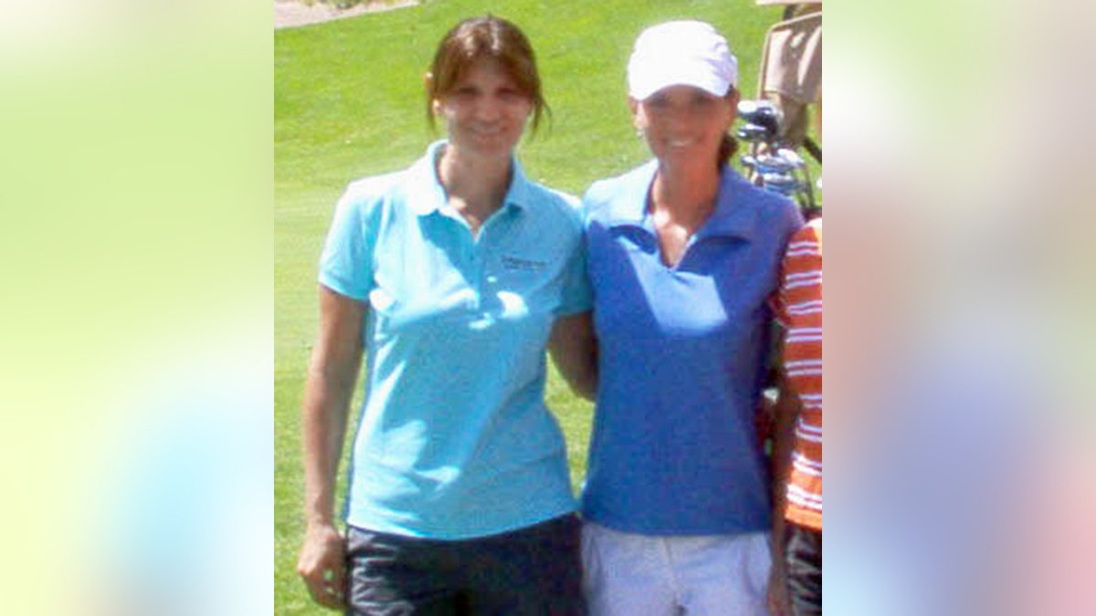 Marie-Anne Thiébaud in an aqua golf shirt and dark pants smiles next to Shania Twain in a light blue golf shirt, white bottoms and white cap on the golf course