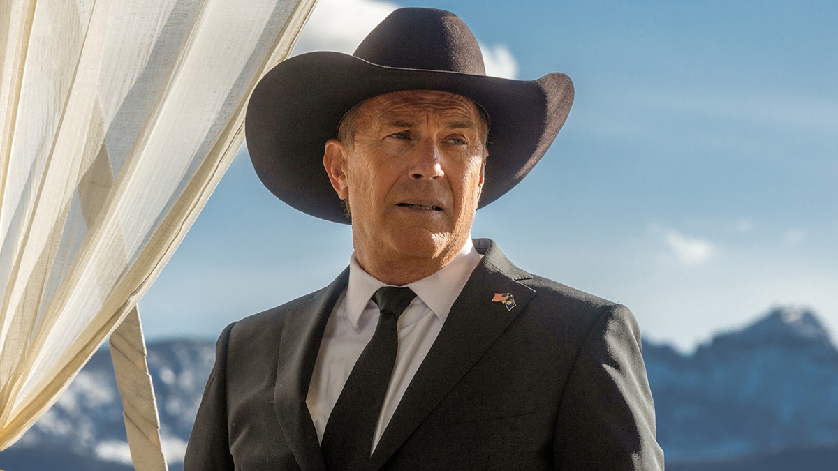 Kevin Costner plays John Dutton in a photo from "yellow stone" wearing a black cowboy hat, suit and tie, looking into the distance