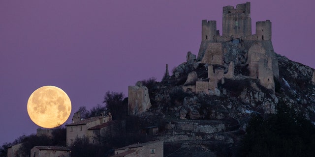 Une pleine lune se couche derrière le château et le village de Rocca Calascio (LAquila), Italie, le 7 mars 2023. La pleine lune de mars est également connue sous le nom de lune de ver, car elle coïncide avec la période de l'année où les vers de terre commencent à émerger de le sol. 