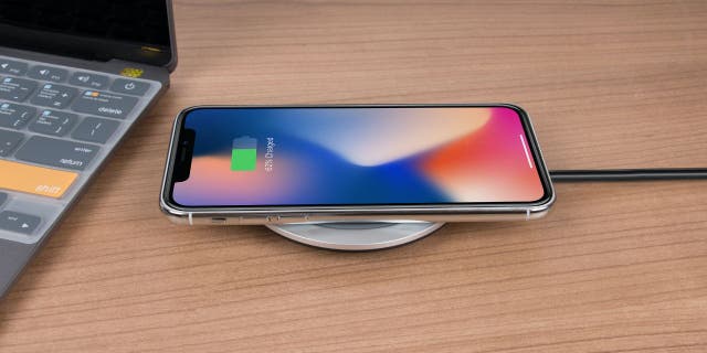 An iPhone charging on a desk. Apple iOS 16.1 has a new update with a clean energy feature.