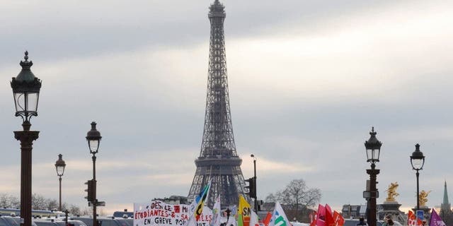 Protesters hold banners as they gather on the Place de la Concorde near the National Assembly, with the Eiffel Tower in the background, to protest after French Prime Minister Elisabeth Borne delivers a speech announcing the use of Article 49.3, a special clause in the French constitution, to pass the pension reform bill to the lower house of parliament without the vote of lawmakers, in Paris, France, March 16, 2023.   