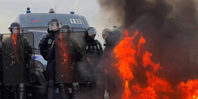 French gendarmes and CRS riot police stand in position near a fire as protesters gather on the Place de la Concorde near the National Assembly in Paris, France, March 16, 2023. 