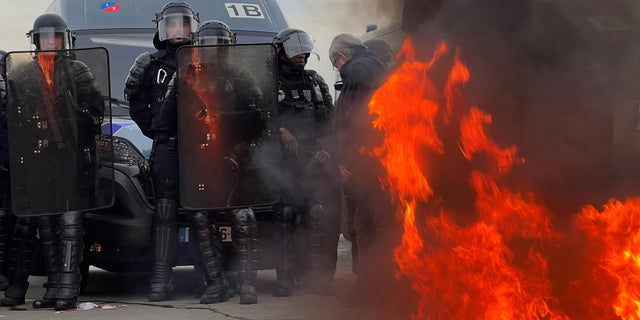 French gendarmes and CRS riot police stand on position near a fire as demonstrators gather on Place de la Concorde near the National Assembly in Paris, France, March 16, 2023.