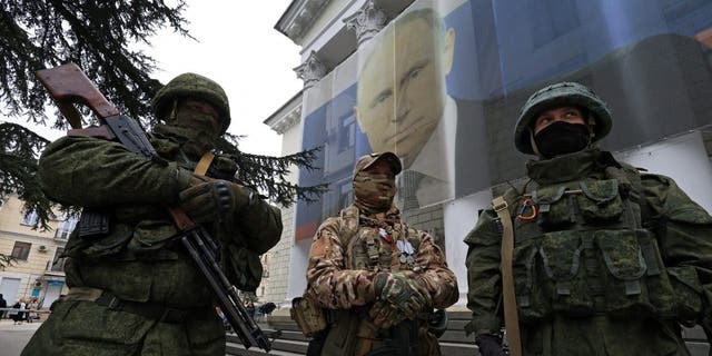 Participants dressed in military uniform stand in front of a banner with a portrait of Russian President Vladimir Putin during a patriotic flash mob marking the ninth anniversary of Russia's annexation of Crimea, in Yalta.