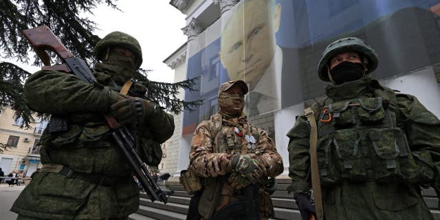 Participants dressed in military uniform stand in front of a banner with a portrait of Russian President Vladimir Putin during a patriotic flash mob marking the ninth anniversary of Russia's annexation of Crimea, in Yalta.