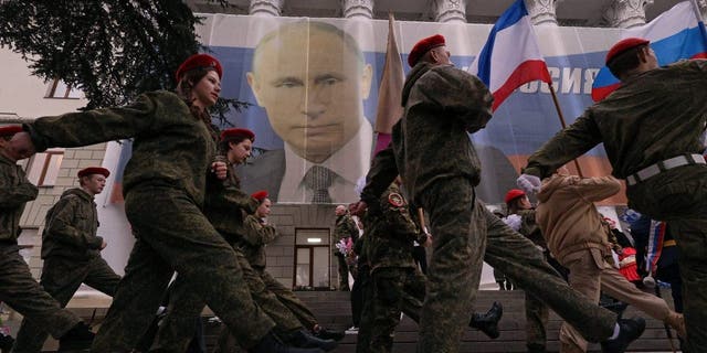 Participants march in front of a banner with a portrait of Russian President Vladimir Putin in a patriotic flash mob marking the ninth anniversary of Russia's annexation of Crimea, in Yalta, Crimea, March 17, 2023.