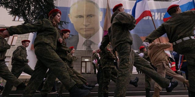 Participants march in front of a banner with a portrait of Russian President Vladimir Putin during a patriotic flash mob marking the ninth anniversary of Russia's annexation of Crimea, in Yalta, Crimea March 17, 2023.