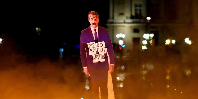 A protester holds a cut-out depicting French President Emmanuel Macron near fire during a demonstration on Place de la Concorde to protest the use by French government of the article 49.3, a special clause in the French Constitution, to push the pensions reform bill through the National Assembly without a vote by lawmakers, in Paris, France, March 17, 2023. 