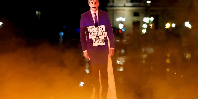 A protester holds a cut-out depicting French President Emmanuel Macron near fire during a demonstration on Place de la Concorde to protest the use by French government of the article 49.3, a special clause in the French Constitution, to push the pensions reform bill through the National Assembly without a vote by lawmakers, in Paris, France, March 17, 2023.