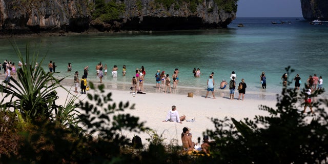 Tourists enjoy the beach during an hour-long visit, where swimming is forbidden and people are only allowed to enter water up to their knees, in Maya Bay at the Phi Phi Island National Park, in Phi Phi Leh Island, Krabi province, Thailand, Feb. 24, 2023. On any given day in Maya Bay, up to 40 blacktip reef sharks cruise in the cyan shallows while about 4,000 tourists visit its white-sand beach flanked by towering cliffs.