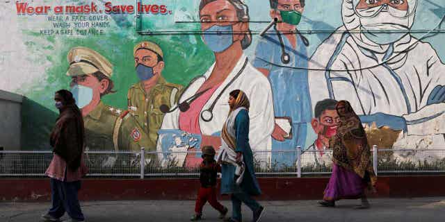 Women walk past graffiti amidst the spread of the coronavirus disease in New Dehli, India. The capital city is ramping up testing for the virus after an increase in cases.