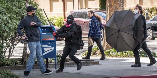 A man carrying a camera is attacked by a Pride Was A Riot trans activist outside the California State Capitol.