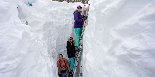 Working inside a nearly 18-foot-deep snow pit at the UC Berkeley Central Sierra Snow Lab, from left, Shaun Joseph, Claudia Norman, Helena Middleton take measurements of snow temperatures ahead of a weather storm on March 9, 2023, in Soda Springs, California.
