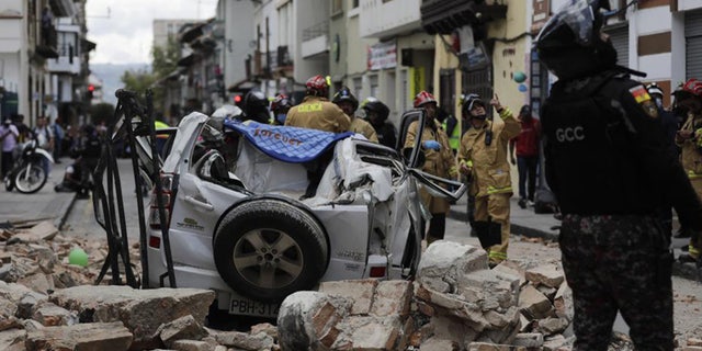 A police officer looks next to a car crushed by debris after an earthquake struck Cuenca, Ecuador, Saturday, March 18, 2023.