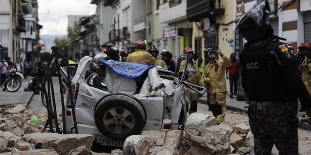 A police officer looks up next to a car crushed by debris after an earthquake shook Cuenca, Ecuador, Saturday, March 18, 2023.