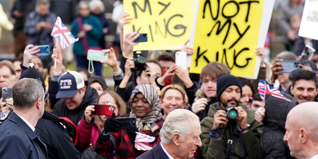 Demonstrators hold placards reading "Not My King" as Britain's King Charles III (C) meets well-wishers upon arriving at the Church of Christ the Cornerstone in Milton Keynes, north of London on February 16, 2023, to attend a reception to mark Milton Keynes' new status as a city. 