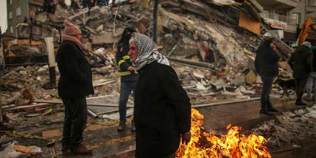 People warm themselves next to a collapsed building in Malatya, Turkey, on Feb. 7, 2023. Turkey will still hold its elections in May even after the devastating earthquake last month.