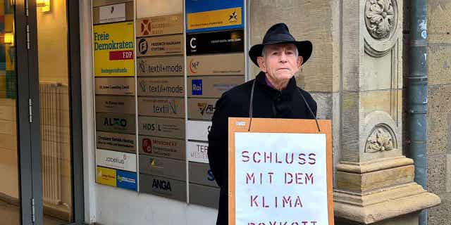 Father Reinhart Kraft of the poses with a protest poster in front of the headquarters of the German Liberal Party in Berlin, Germany, on March 3, 2023.
