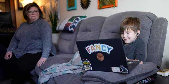 A mother watches as her 6-year-old son works with a tutor on his laptop in Indianapolis, on March 7, 2023. 