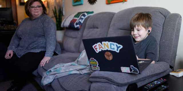 A mother watches as her 6-year-old son works with a tutor on his laptop in Indianapolis, on March 7, 2023.