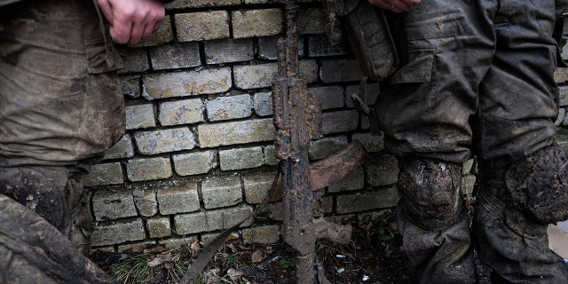 A mud-stained gun is seen in front of Ukrainian servicemen which just come back from tranches of Bakhmut in Chasiv Yar, Ukraine, Wednesday, March 8, 2023. 