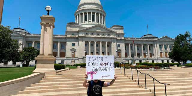 A demonstrator holds a sign outside the Arkansas state Capitol in Little Rock on June 24, 2022, protesting the overturning of Roe v. Wade. A monument marking the number of abortions performed in Arkansas is being sent to Gov. Sarah Huckabee Sanders on March 14, 2023. 