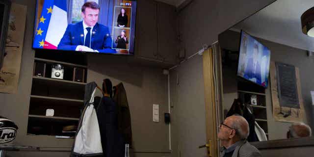 A man watches French President Emmanuel Macron speak during an interview with journalists on television in Marseille, France, on March 22, 2023. Macron said the controversial pension bill should be implemented by the "end of the year."
