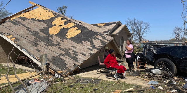 People sit in front of a damaged home on Saturday in Silver City, Miss. At least 25 people were killed in the state after a tornado ripped through several towns.